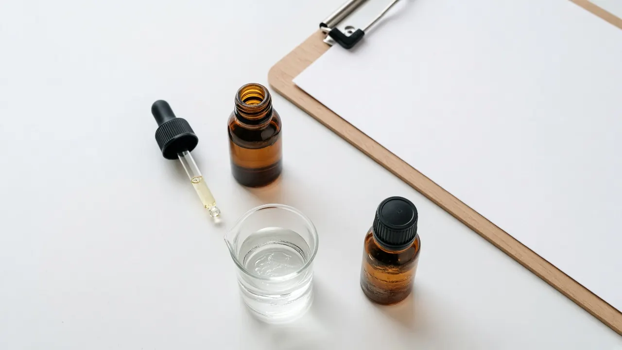 Two amber oil bottles, a clear gel beaker, a dropper, and a clipboard on a white bench